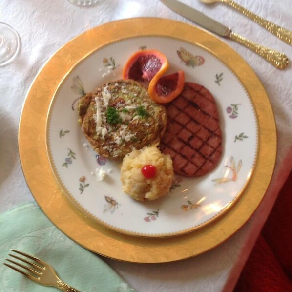 Um prato com alimentos, incluindo um hambúrguer grelhado, um item frito e uma pequena porção com uma cereja.