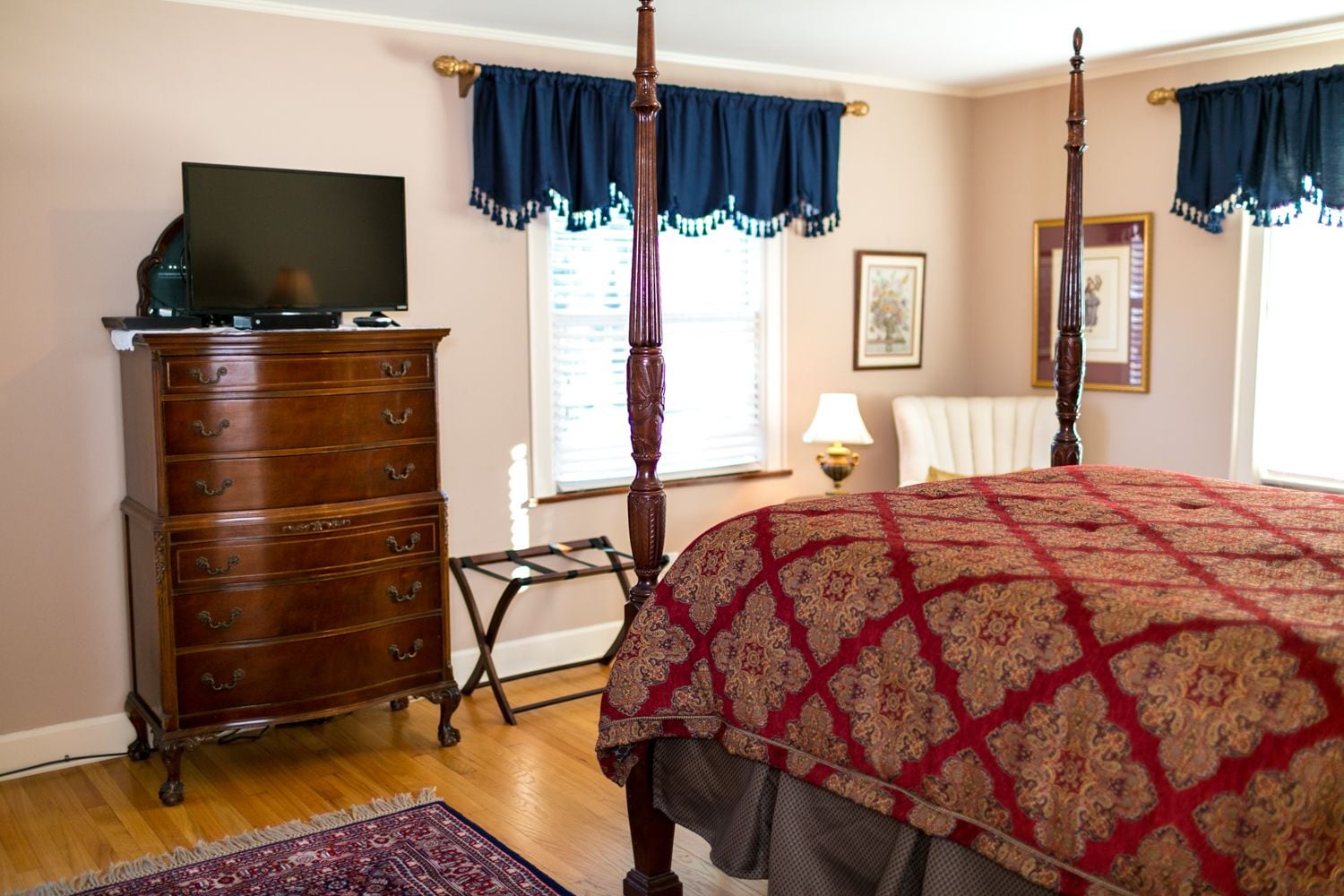 Un dormitorio con una cama con dosel, un aparador de madera, un televisor encima y una ventana con cortinas.