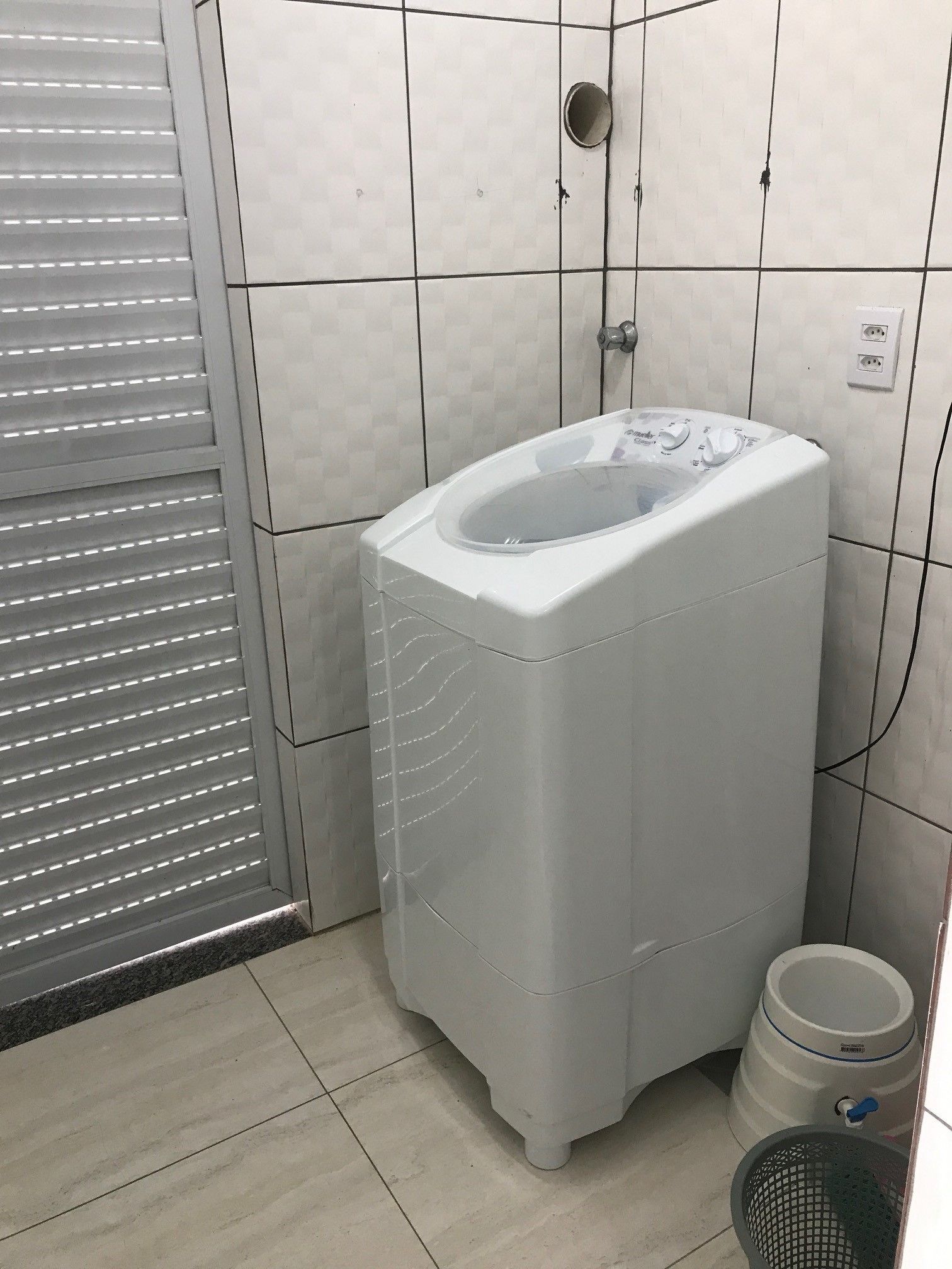 A compact, white washing machine in a bathroom with tiled walls and a tiled floor.