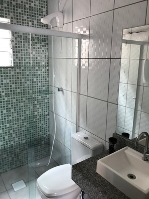 Casa de banho com cabine de duche em vidro, sanita, lavatório e espelho.