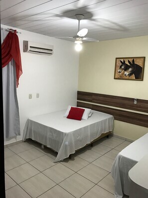 Quarto individual com ventoinha no teto, ar condicionado, cortina vermelha, quadro de burros pendurado na parede e mesa de cabeceira.