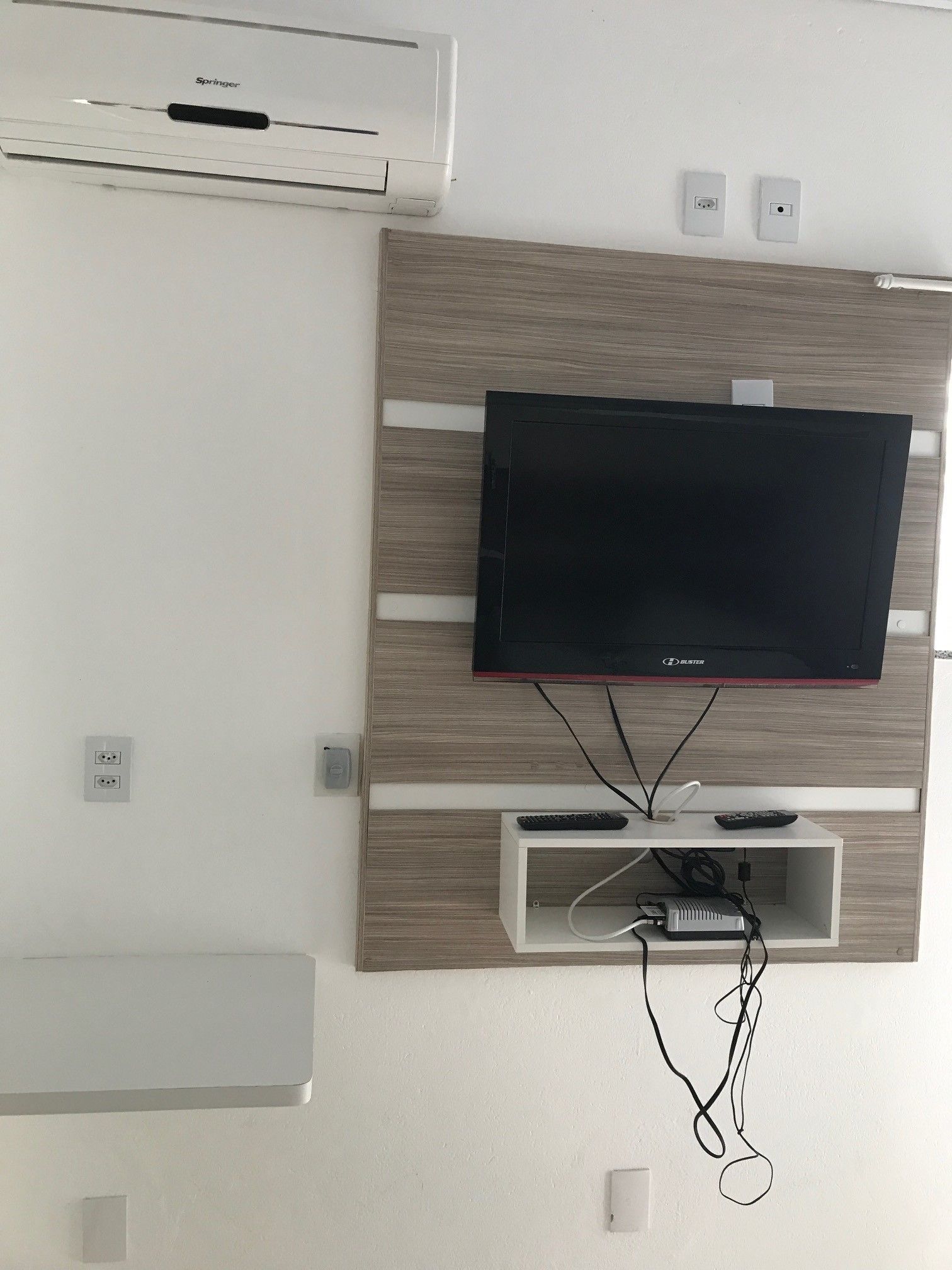 A wall-mounted flat-screen TV on a wooden panel with a cable management system below.