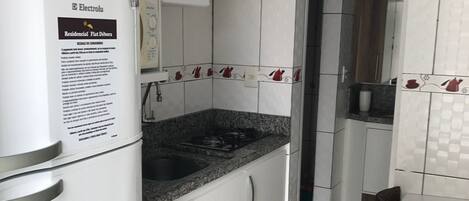 A kitchen with white cabinets, a refrigerator, a sink, and a dining area with a table and chairs.