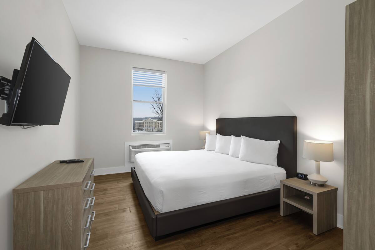 Un dormitorio moderno con una cama grande, mesitas de noche, un televisor y una ventana con persianas.