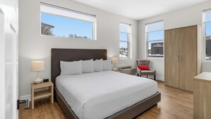 A modern bedroom with a large bed, bedside tables, a chair, and a wardrobe. - Lake Placid Inn Main Street (Lake Placid)