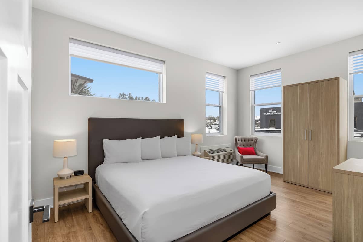 Un dormitorio moderno con una cama grande, mesitas de noche, una silla y un armario.