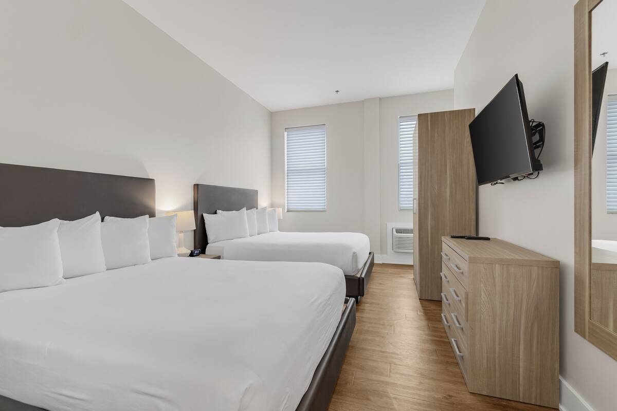 Una habitación de hotel con dos camas, un televisor montado en la pared y un aparador de madera.