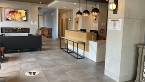 A modern interior with a reception desk, seating area, and a television displaying food. - Lake Placid Inn Main Street (Lake Placid)