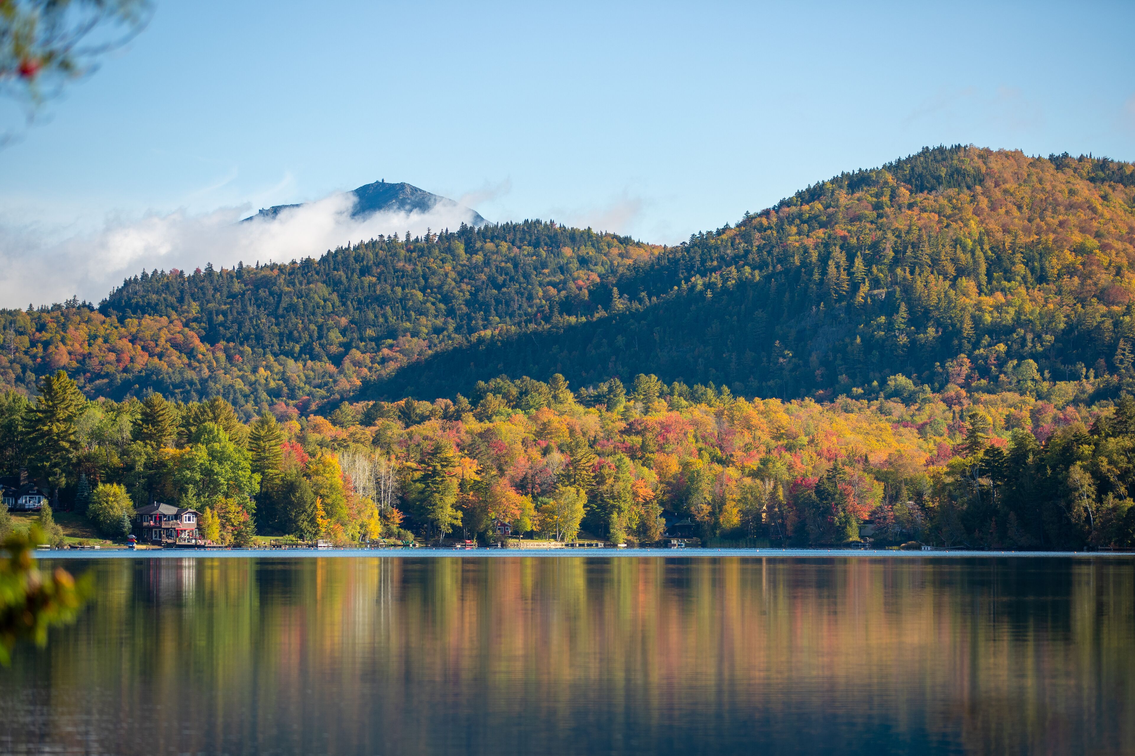 Ruhiger See mit Bergblick, ein Haus am Wasser und klarer Himmel.