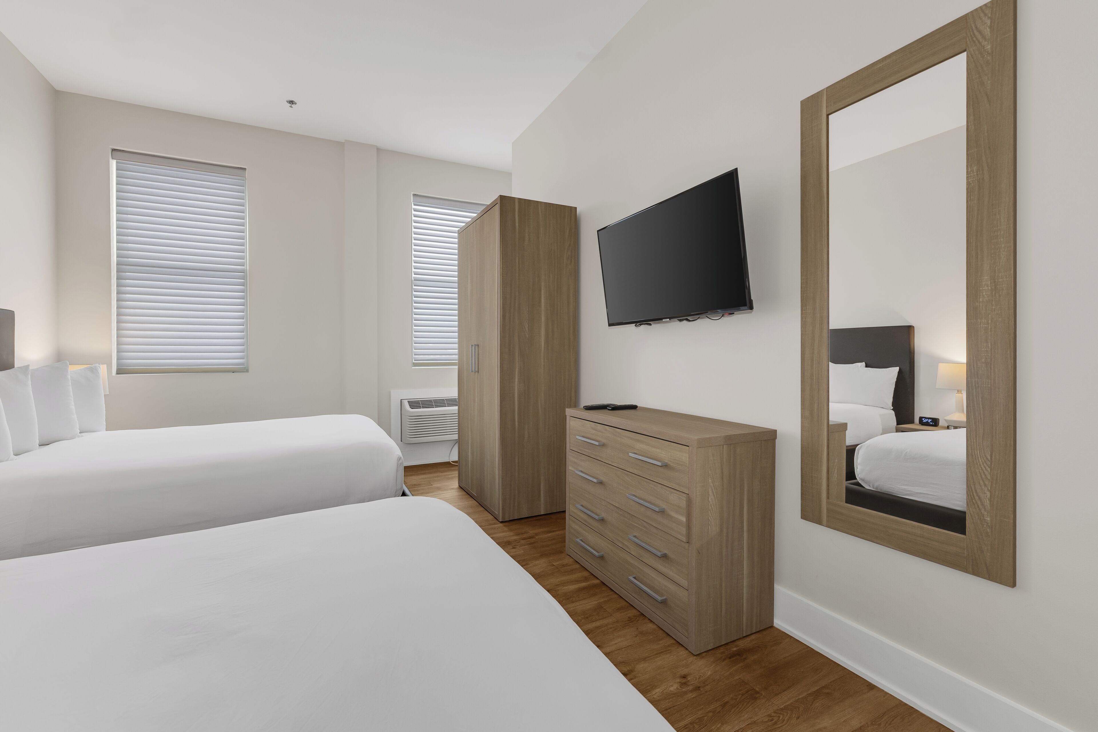Une chambre d’hôtel avec deux lits, une télévision, une commode et un grand miroir.