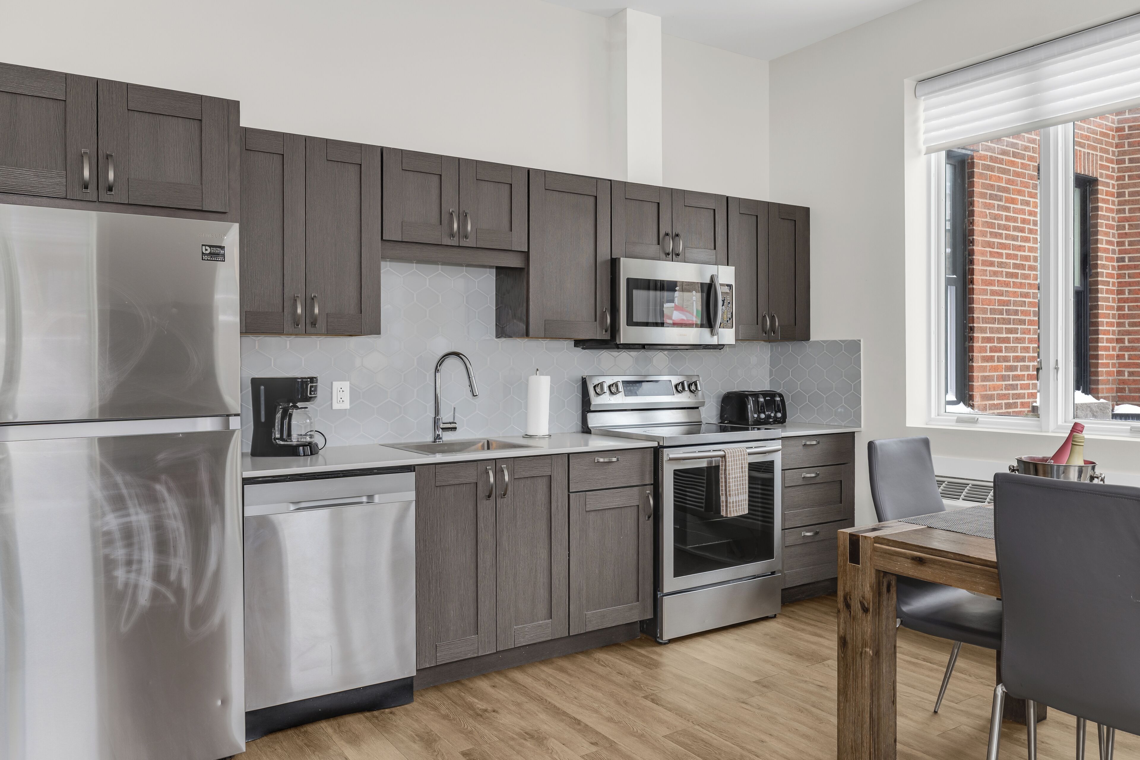 Una cocina moderna con electrodomésticos de acero inoxidable, gabinetes grises y una mesa de comedor de madera.
