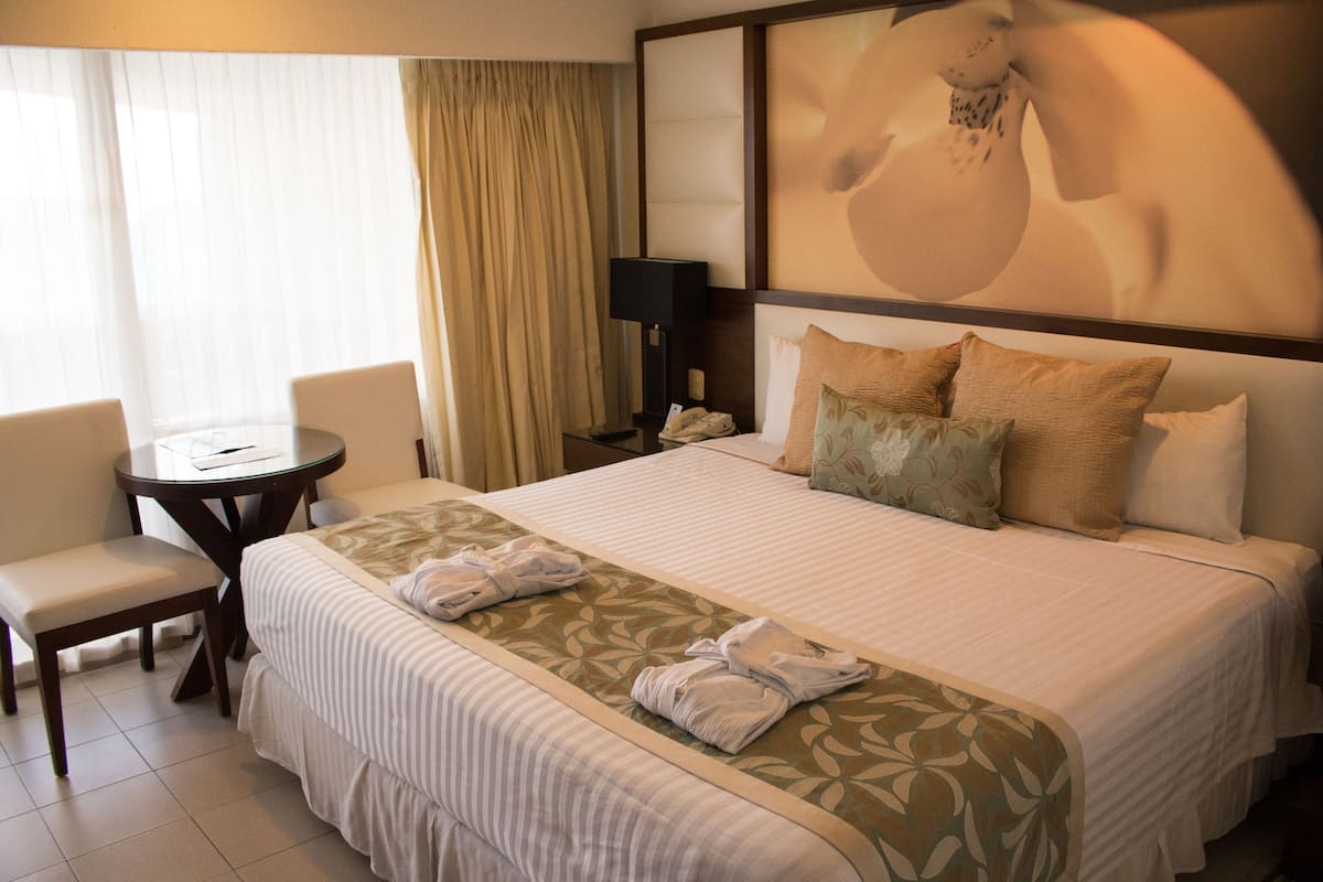 A hotel room with a large bed, a bedside table, a chair, and a lamp.