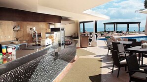 A modern kitchen with a bar area, a poolside lounge with chairs and tables, and a view of the ocean. - Club GR Caribe Cancun – Premier All Inclusive (Cancun)