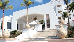 A white building with a staircase leading to an entrance, surrounded by palm trees and decorative vases. - Club GR Caribe Cancun – Premier All Inclusive (Cancun)