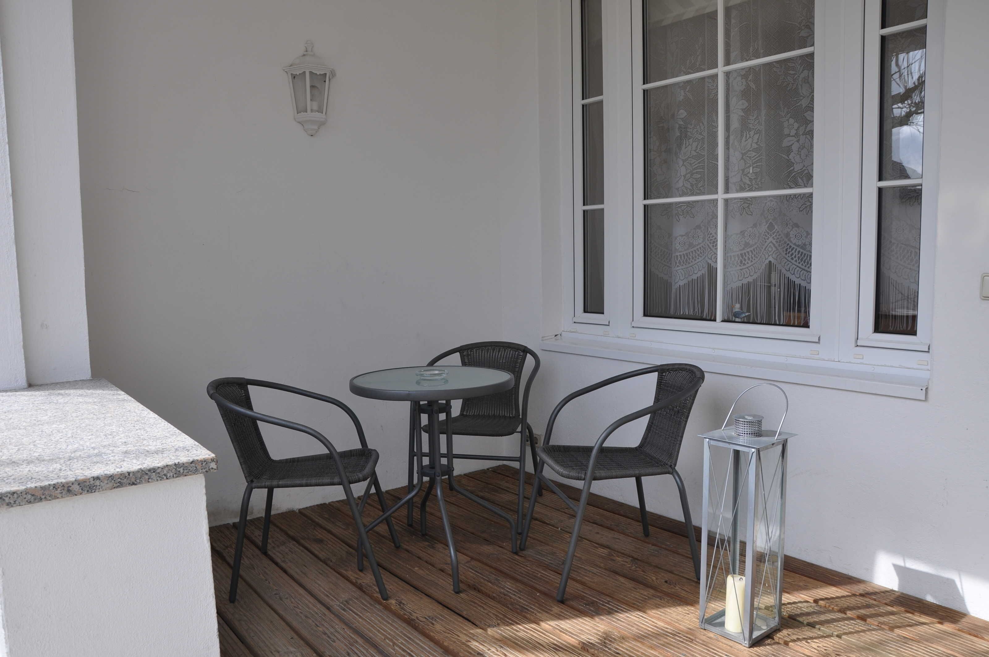 A patio with a round table and four chairs, a lantern, and a window with patterned curtains.