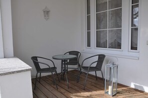 Een terras met een ronde tafel en vier stoelen, een lantaarn en een raam met decoratieve gordijnen.