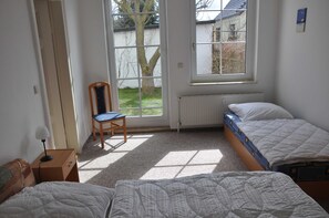 Une chambre avec deux lits, une chaise, un bureau avec une lampe et une fenêtre donnant sur l’extérieur.