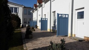 Un pati amb paviment de pedra, edificis blancs i portes blaves.