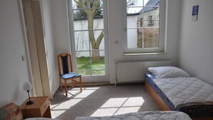 A bedroom with two beds, a chair, a desk with a lamp, and a window with a view of the outside. - Apartment Gording II - Holiday residence sea desire (Koserow)