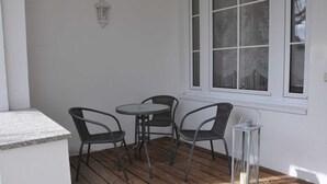 A patio with a round table and four chairs, a lantern, and a window with patterned curtains. - Apartment Gording II - Holiday residence sea desire (Koserow)