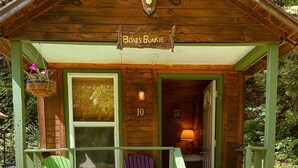 A wooden cabin with a porch, numbered 10, featuring two green Adirondack chairs and a purple Adirondack chair. - Pine Crest Motel And Cabins (Barton)