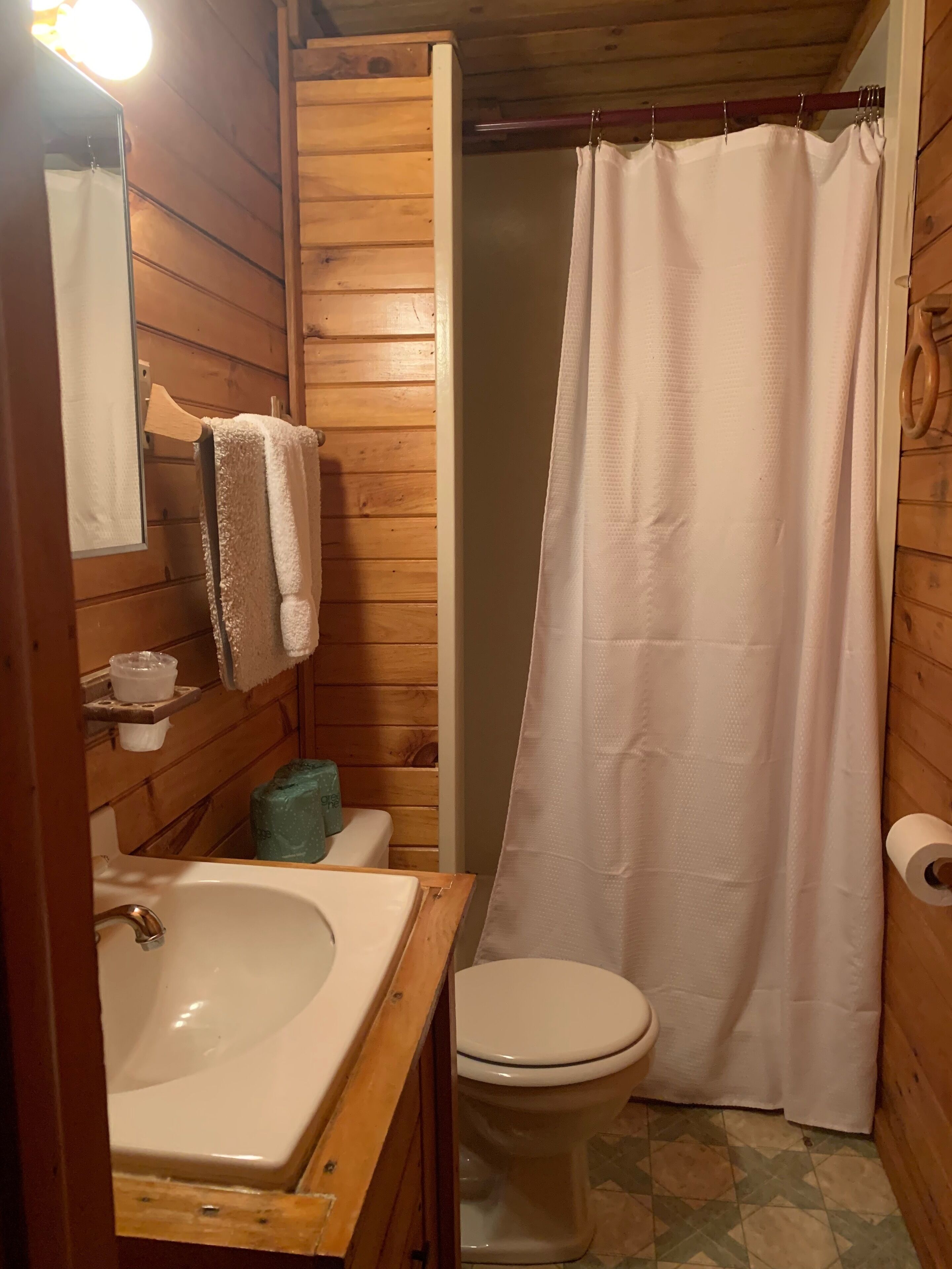 A wooden bathroom with a white sink, toilet, and shower curtain.