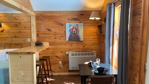 A wooden interior with a kitchen area, a dining table with chairs, and a painting on the wall. - Pine Crest Motel And Cabins (Barton)