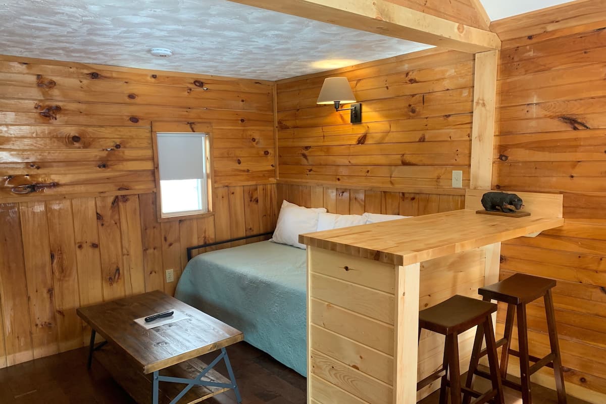A cozy cabin room with a bed, a small desk, and a bar area.