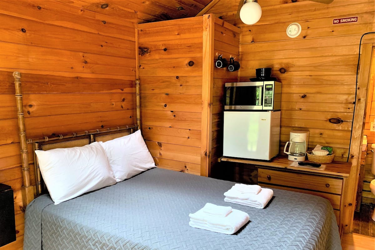 A wooden cabin room with a bed, a refrigerator, a microwave, and a coffee maker.