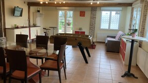 Una sala de estar acogedora con mesa de fútbol, comedor con sillas y mesa, y cocina con refrigerador y televisor.