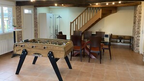Una habitación acogedora con una mesa de futbolín, sillas de madera, una escalera y una pared de ladrillo.