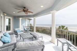 A covered outdoor seating area with a view of the ocean, featuring a ceiling fan, white columns, and a railing. - 37 Dune Lane - Island Dream Home, 7 Bedroom Oceanfront (Hilton Head Island)