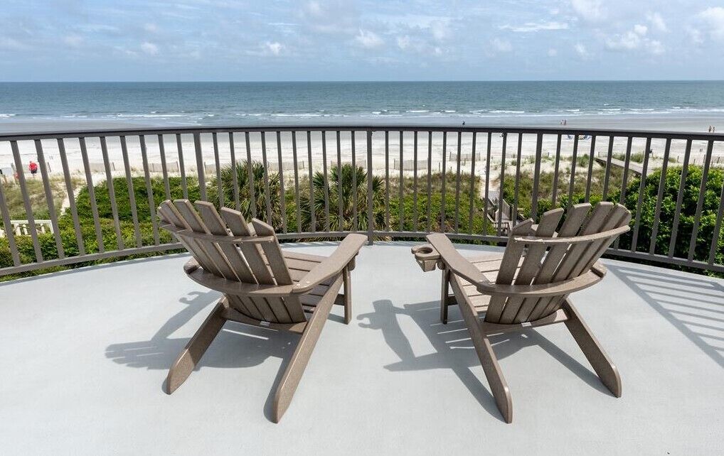 A balcony with two Adirondack chairs facing a beach.
