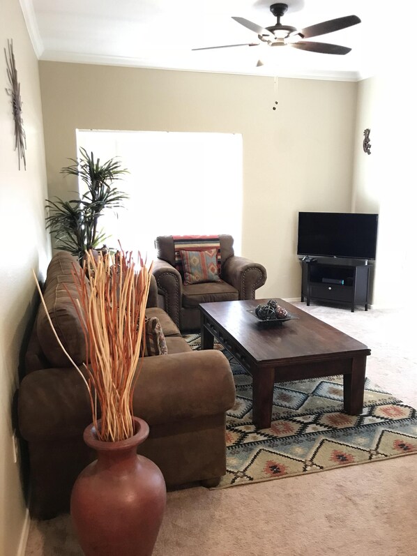 A living room with a sofa, a coffee table, a TV stand, and a ceiling fan.