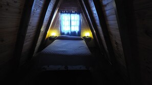 Una habitación estrecha con paneles de madera, una cama, dos lámparas de noche y un ventanal con cortinas.