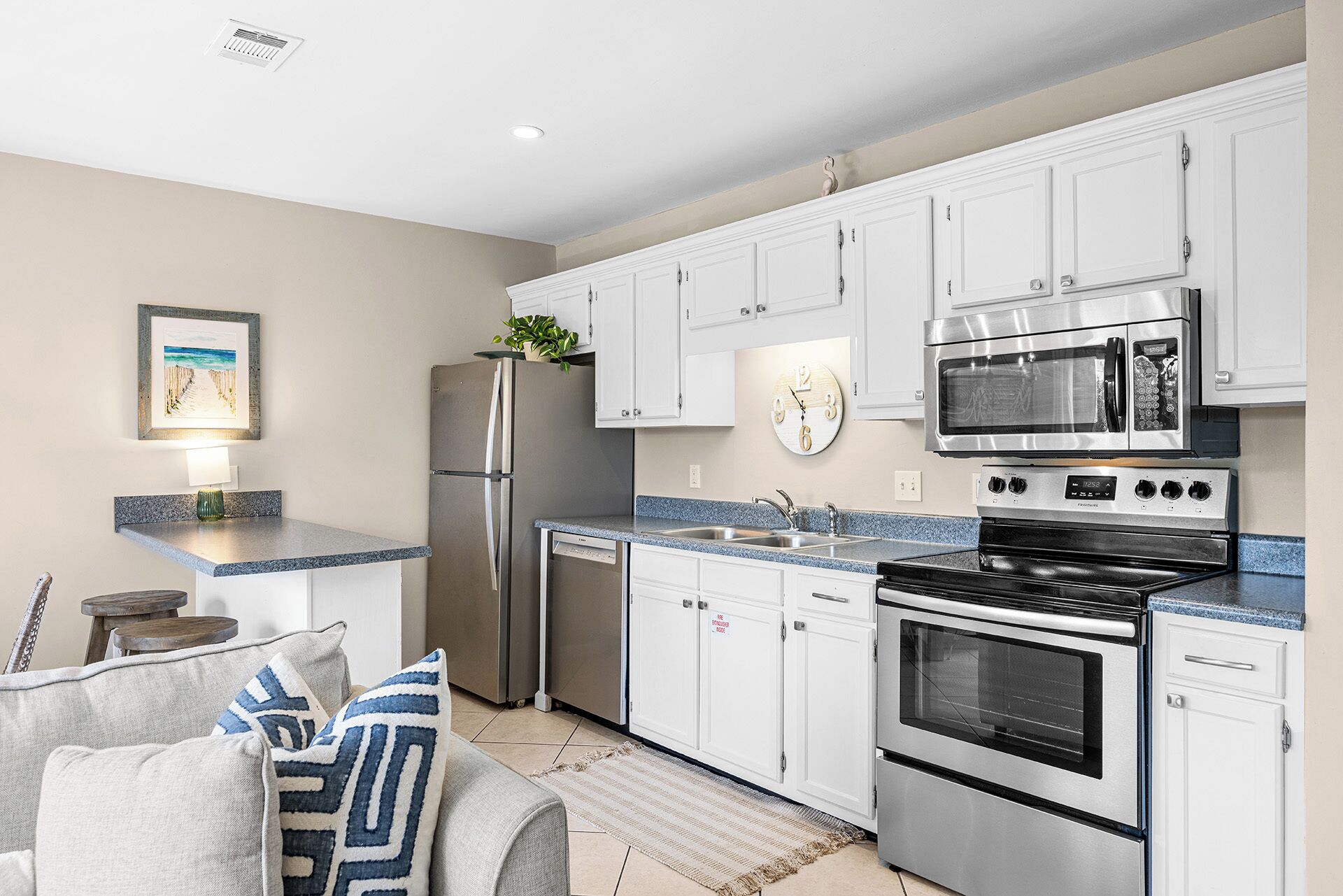 A modern kitchen with white cabinets, stainless steel appliances, a clock, and a framed picture on the wall.
