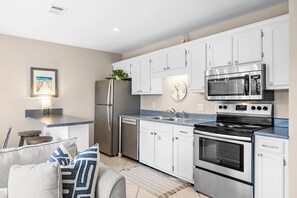 A modern kitchen with white cabinets, stainless steel appliances, a clock, and a framed picture on the wall.