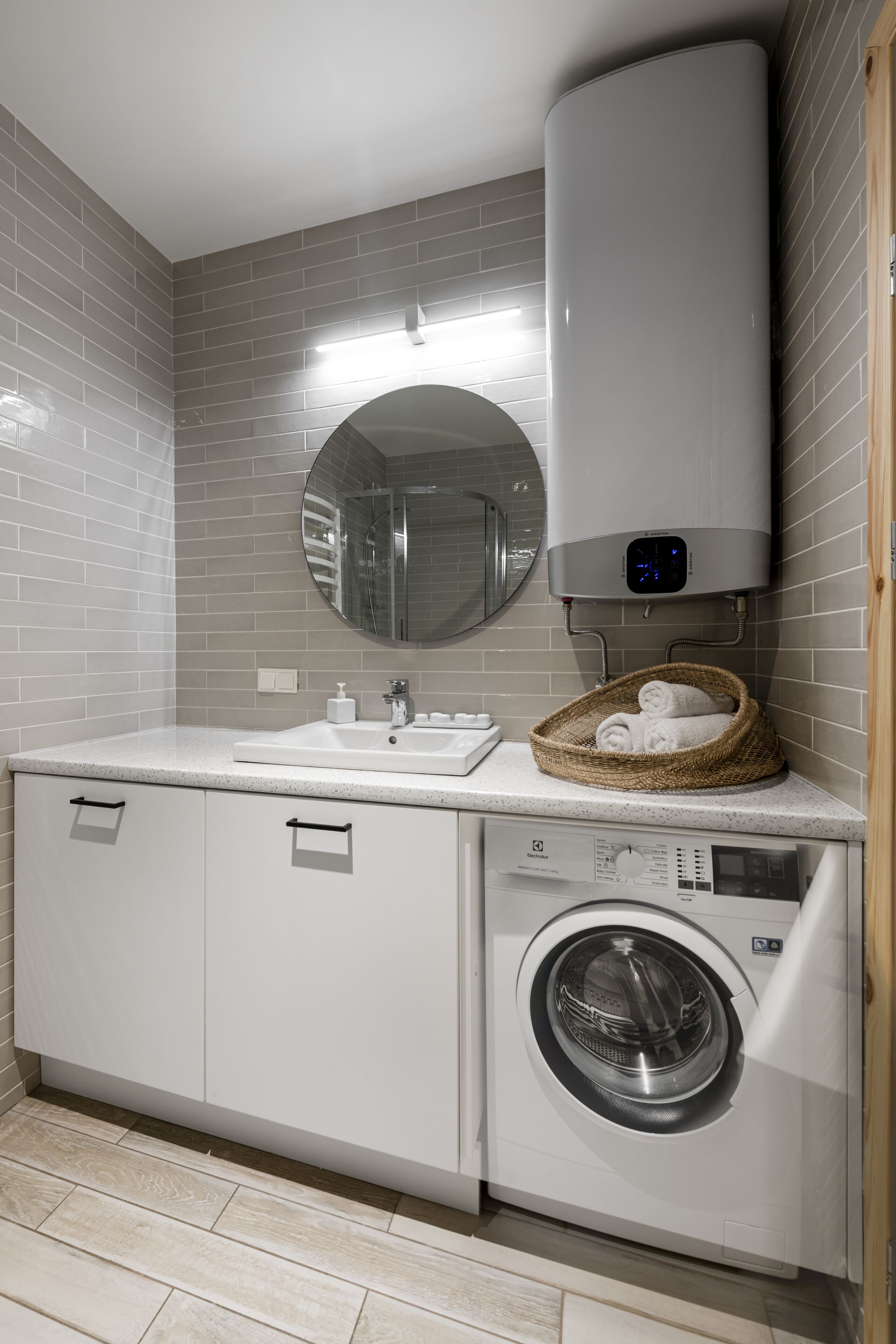 A compact bathroom with a washing machine, a sink, and a mirror.