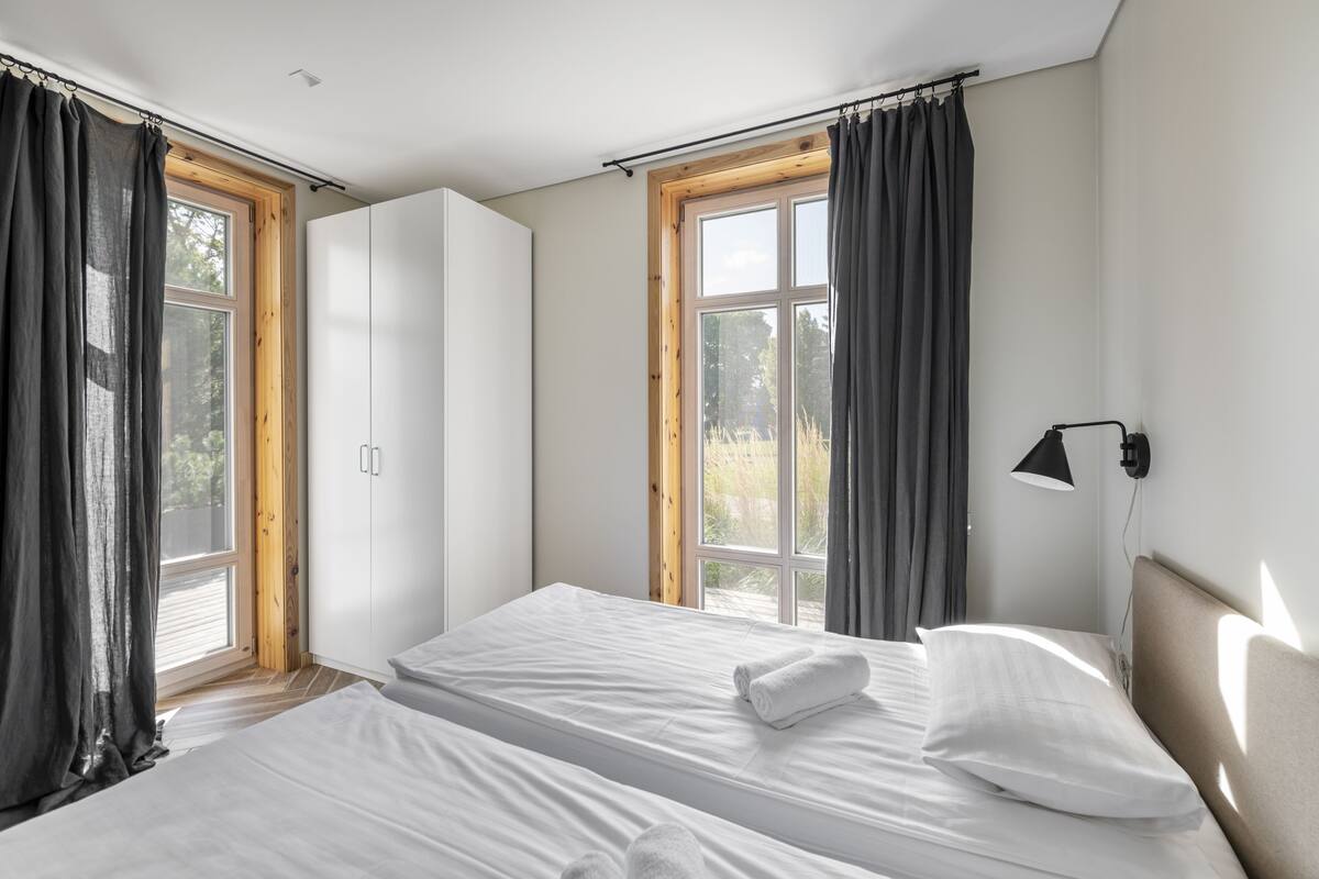 A bedroom with two beds, a wardrobe, and a window with curtains.