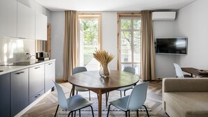 A modern kitchen with a dining area, a flat-screen TV, and a large window with curtains. - Uz Juru Mariu (Neringa)