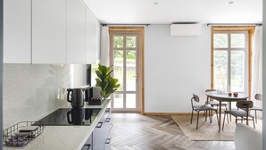 A modern kitchen with a herringbone floor, a dining area with a round table and chairs, and a large window with a view of greenery. - Uz Juru Mariu (Neringa)