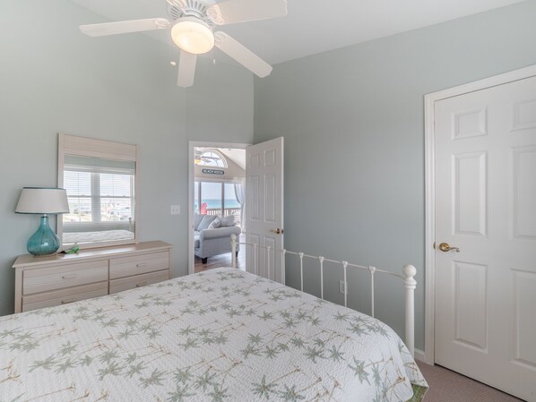 A bedroom with a bed, a dresser, a ceiling fan, and a door leading to a balcony.