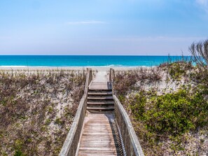 A wooden boardwalk leading to a beach with clear blue water.