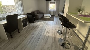 Moderni olohuone, jossa on sohva, ruokailutila baarituoleineen sekä työtila työpöydällä ja tuolilla.
