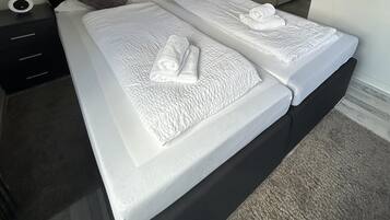 A double bed with white linens and two pillows, a bedside table with a lamp, and a wardrobe in the background.
