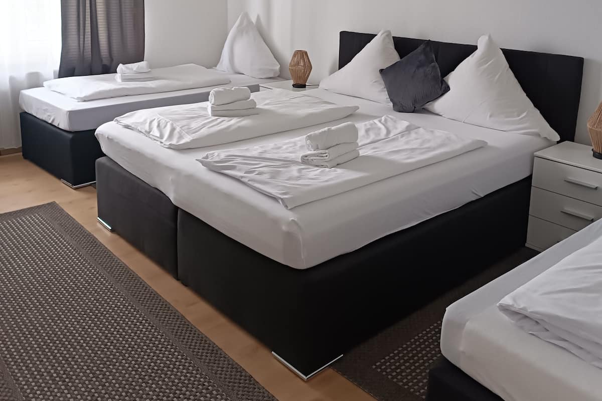 Una habitación de hotel moderna con dos camas, una mesita de noche y un ventanal con cortinas translúcidas.