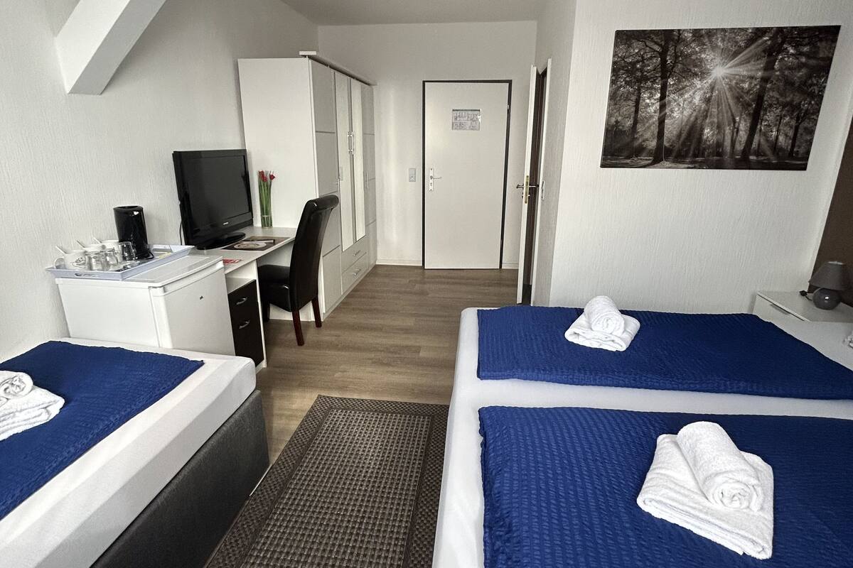 Habitación de hotel con dos camas, un escritorio con ordenador, televisión y un cuadro en la pared.