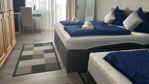 Hotellihuone, jossa on kaksi sänkyä, työpöytä, tuoli ja vaatekaappi.