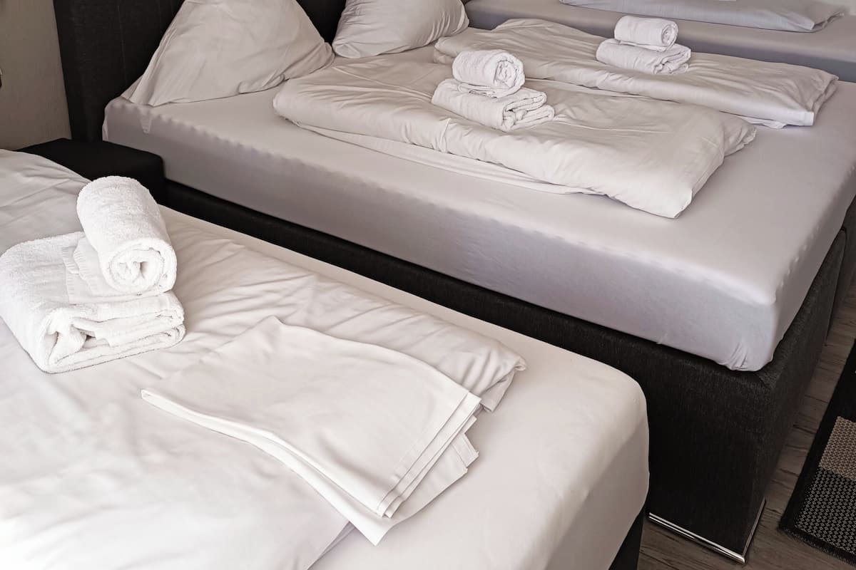 Habitación de hotel con tres camas individuales, cada una con una toalla blanca doblada con cuidado.