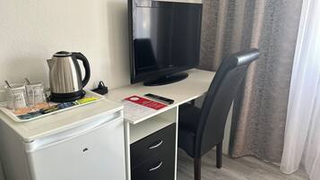 A compact hotel room with a kitchenette, a flat-screen TV, a black office chair, and a small desk.